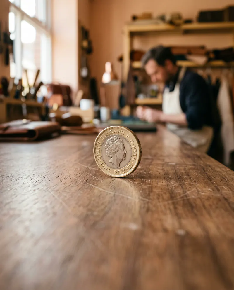 A single pound coin standing on its edge on a walnut desk, softly lit