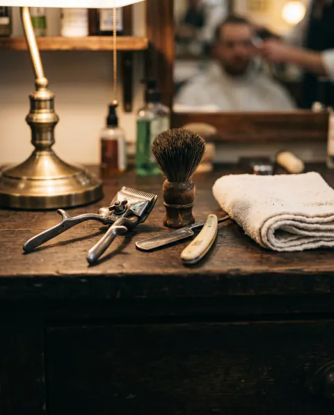 Vintage barber clippers and a straight razor laid out on a dark wooden counter